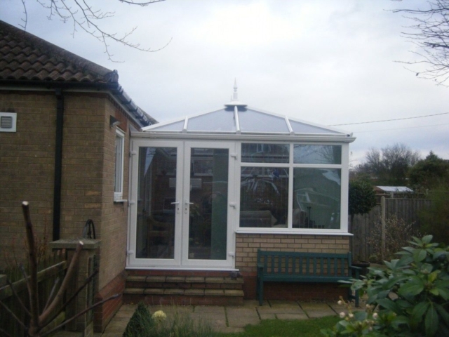 Small white and brick Edwardian-style conservatory attached to a home