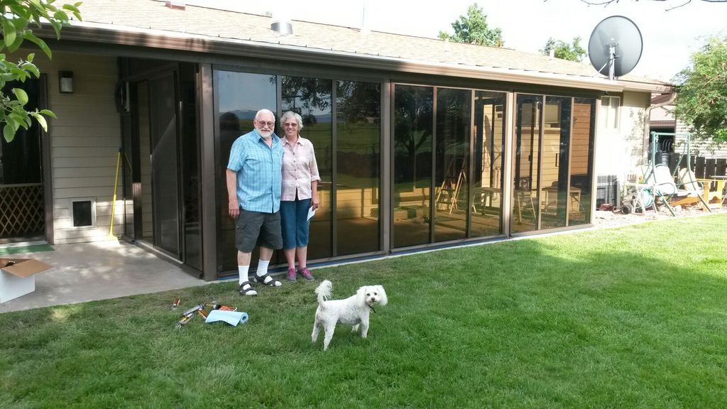 Two people outside of a brown solarium attached to back of house with white dog